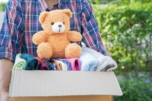 sosteniendo una caja de donación de ropa con ropa usada y muñecas en casa para apoyar la ayuda a los pobres del mundo. foto