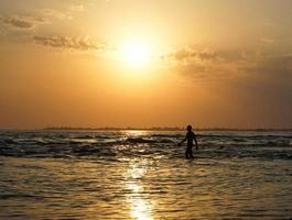 paisaje marino con una magnífica puesta de sol y la silueta de un hombre caminando sobre el mar. foto