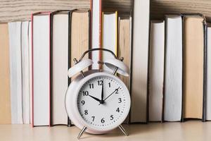 white alarm clock showing 10 o clock front bookshelf wooden desk photo