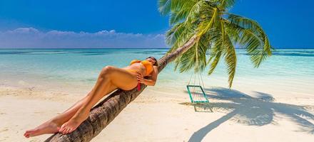 Vacation on the seashore. Young woman in black swimsuit on the beautiful tropical beach laying on the palm tree.