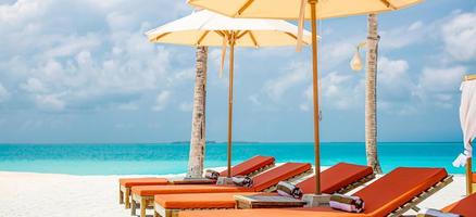 Escena tranquila de playa con hamacas bajo cocoteros cerca de la piscina y la laguna del océano. arena blanca, clima soleado, concepto de hotel resort de vacaciones de verano