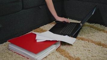 laptop in de woonkamer op de grond, op het tapijt, met veel werk- of studiedocumenten.