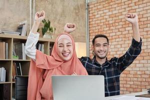 Los socios de startups jóvenes que son personas islámicas se sientan en un escritorio, levantan la mano para felicitar el éxito de las pequeñas empresas de comercio electrónico de oficinas. dos pares de colegas sonríen y están felices de trabajar. foto