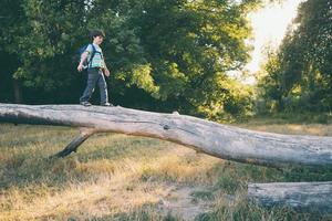A boy with a backpack walks along the trunk of a fallen tree, a child learns to keep his balance photo
