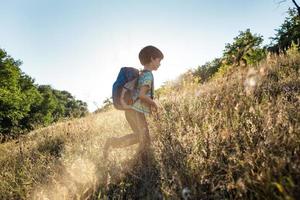 un niño con una mochila camina en el prado foto