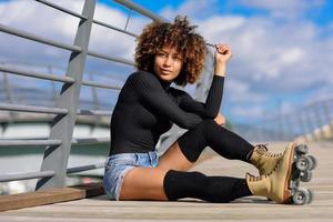 Afro hairstyle woman on roller skates sitting on urban bridge