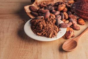 Cocoa powder and cocoa beans with cocoa pods on wooden background. photo