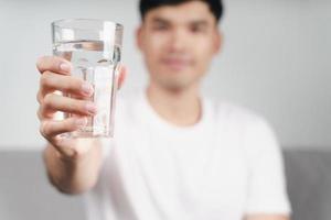 handsome asian man drinking a glass of water on the sofa at living room photo