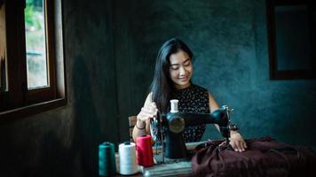 chica asiática disfrutando y sentado con máquina de coser con máquina de coser antigua. foto