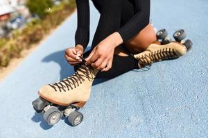 irreconocible niña negra sentada en la línea de la bicicleta y se pone patines foto