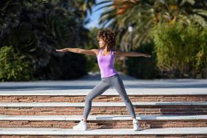 mujer negra, peinado afro, haciendo yoga en pose de guerrero foto