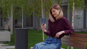 mujer feliz charlando y gesticulando durante la videollamada en línea desde el parque de la ciudad.