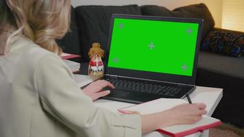 Woman writing and using laptop with green screen in home office video