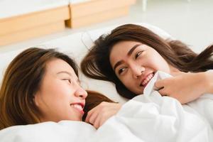 Top view of beautiful young asian women lesbian happy couple showing surprise and looking at camera while lying in bed under blanket. Funny women after wake up. Lesbian couple together indoors concept photo