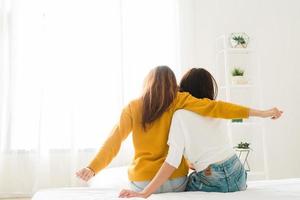 Vista posterior de la pareja feliz lesbiana de las mujeres que se despierta por la mañana, sentada en la cama, estirándose en el dormitorio acogedor, mirando por la ventana. mujeres divertidas después de despertar. pareja de lesbianas lgbt juntos en el interior concepto foto