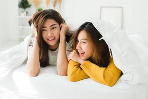 Vista superior de hermosas mujeres asiáticas jóvenes lesbianas pareja feliz mostrando sorpresa y mirando a la cámara mientras está acostado en la cama debajo de la manta. mujeres divertidas después de despertar. pareja de lesbianas, juntos, en el interior, concepto foto
