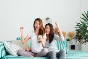 LGBT lesbian women couple moments happiness. Lesbian women couple together indoors concept. Friends young smiling women at home sitting on the couch and watching tv, She is holding a remote control. photo
