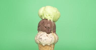 Front view, Melting of three ice cream balls on the cone. Different flavors of ice cream flow from the cones. On the green background. video