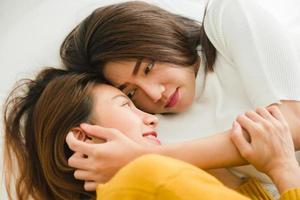 Beautiful young asian women LGBT lesbian happy couple hugging and smiling while lying together in bed under blanket at home. Funny women after wake up. LGBT lesbian couple together indoors concept. photo