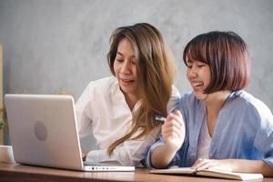 Two young business women sitting at table in cafe. Asian women using laptop and cup of coffee. Freelancer working in coffee shop. Working outside office lifestyle. One-on-one meeting. photo