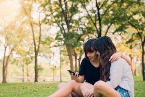 Dos hermosas amigas asiáticas jóvenes felices divirtiéndose juntos en el parque y tomando un selfie. feliz hipster jovencitas asiáticas sonriendo y mirando el teléfono inteligente. conceptos de estilo de vida y amistad. foto