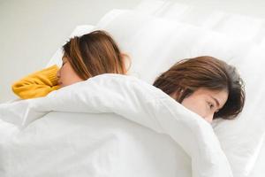 Beautiful young asian women LGBT lesbian happy couple hugging and smiling while lying together in bed under blanket at home. Funny women after wake up. LGBT lesbian couple together indoors concept. photo