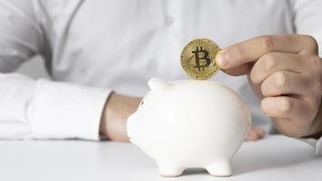 man inserting bitcoin piggy bank photo