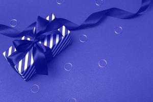 Striped gift box with ribbon and decorations. Tinting in the trendy color of the year, very peri, closeup. photo