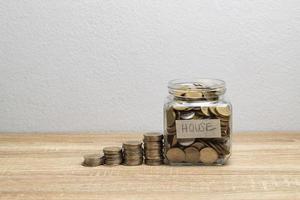 Coin in a glass jar with money stack on the brown table photo