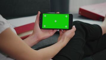 Woman sitting on sofa while looking at movies using phone with mock up green screen display. video