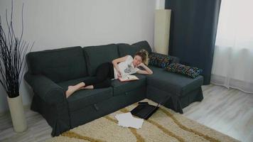 Student woman lying on the couch in the living room studying at home.