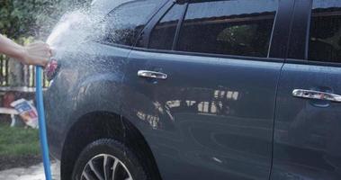 Vista frontal, sostenga la manguera de goma con agua en aerosol y lave el automóvil. Limpiar el coche después de su uso.