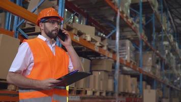 Caucasian employee speaking by mobile phone in storage. video