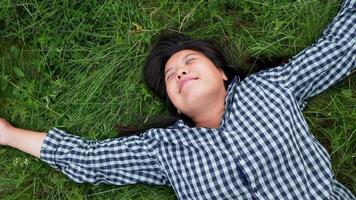 Top view of happy Asian woman taking a rest on grass in a farm. Taking a deep breath and getting some fresh air. Feeling fresh and having happy face. Being in a beautiful green farm video