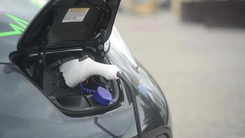 un coche eléctrico que se carga desde la toma de corriente, cargador de coche de calle al aire libre video