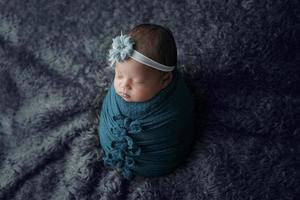 Little newborn baby enveloped in blue scarf with a bandage on his head lies on a soft blanket photo