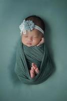 Little newborn baby enveloped in blue scarf with a bandage on his head lies on a soft blanket photo