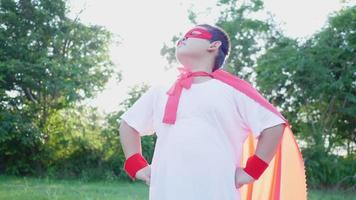 menino gordo asiático vestindo fantasia de herói, pose de braços na cintura e olhando para o céu no parque, usando máscara vermelha e xale. saindo de férias. conceito de fantasia de herói video