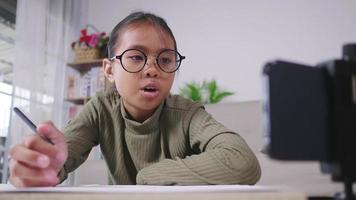 menina asiática sentado e estudando online na sala de estar em casa, lendo a aula no telefone. definindo o smartphone na mesa e estudando on-line pelo conceito de smartphone video