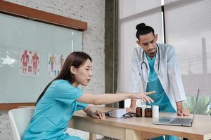 Healthcare team partners. Two uniformed young Asian ethnicity doctors are co-workers discussing medication in hospital's clinic office. Specialist persons are experts and professionals. photo