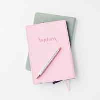 espacio de trabajo blanco con cuaderno rosa claro y flor blanca con café en la mesa blanca. foto