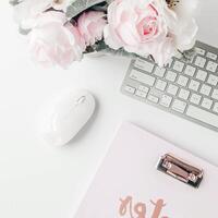 white workspace with light pink note book and white flower with coffee on white table. photo