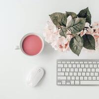 white workspace with light pink note book and white flower with coffee on white table. photo