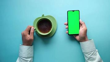 Erhöhte Ansicht der Hand des Mannes mit Smartphone und grünem Tee trinken video