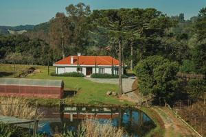 bento goncalves, brasil - 12 de julio de 2019. encantadora casa de campo moderna con camino y lago, en un paisaje boscoso cerca de bento goncalves. foto