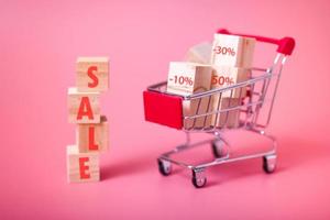 Miniature shopping cart and wooden blocks with sale lettering, isolated pink background. photo