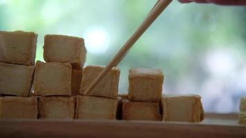 Use chopsticks picking up diced tofu from wood tray against nature background video
