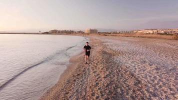 jonge runner man training op prachtige zonsondergang op het strand. drone volgen video