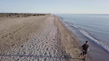 homem jovem corredor treinando no belo pôr do sol na praia. visão do drone video