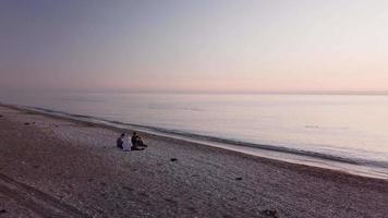 drie vrienden zitten op het strand en kijken naar de zonsondergang video